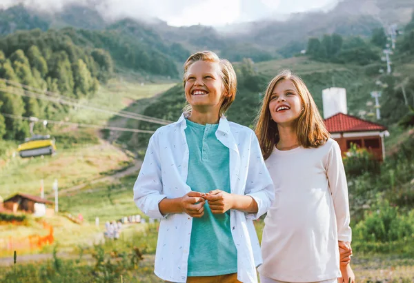 Barn bror och syster vänner ser upp med beundran mot bakgrund av Mountain Resort, familj resor — Stockfoto