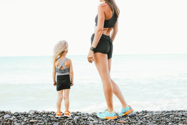 Young fit woman mom with little cute girl exercising on morning  beach together, healthy lifestyle, sport family