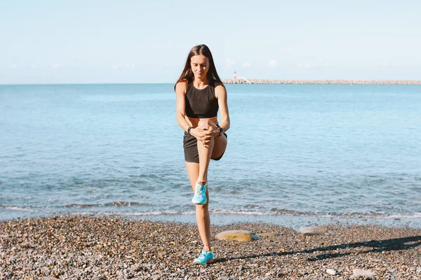 Giovane donna atletica sottile in abbigliamento sportivo facendo esercizi sulla spiaggia al mare al mattino, stile di vita sano — Foto Stock