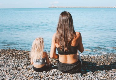 Birlikte plajda oturan küçük sevimli kız ile genç uygun kadın anne, sağlıklı yaşam tarzı, spor aile