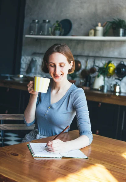 Junge Frau mit Südpfote berechnet Familienbudget, schreibt Tagebuch in der Küche — Stockfoto