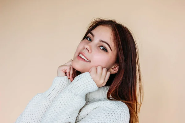 Portret van mooie lachende tiener meisje met schone huid en donker lang haar in gezellige witte trui op beige achtergrond — Stockfoto
