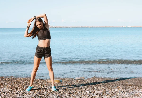 Young slim athletic woman in sportswear doing exercises on the sea beach in morning, healthy lifestyle — Stock Photo, Image