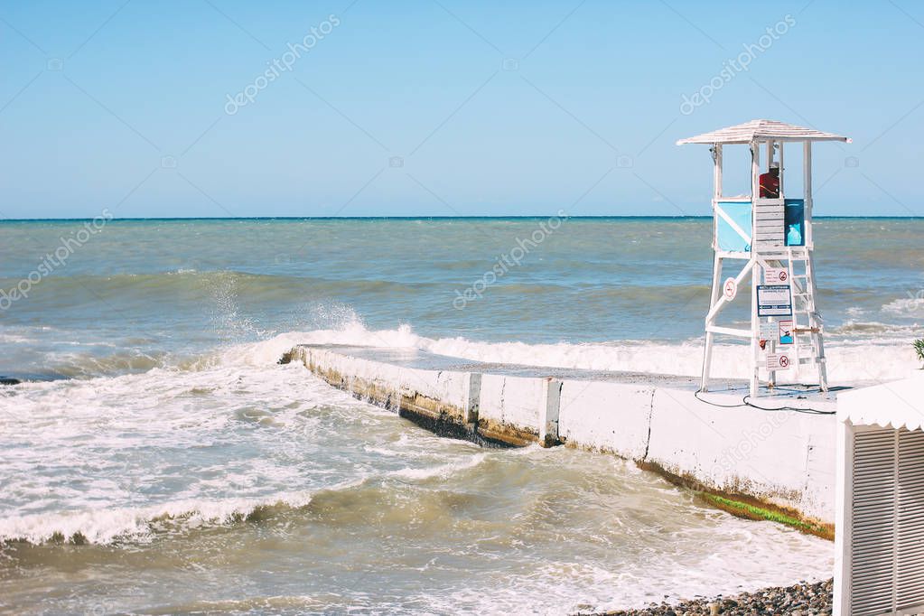 Sochi, Russia - August, 05, 2019. White booth tower with lifeguard on shore of storming Black sea, empty beach