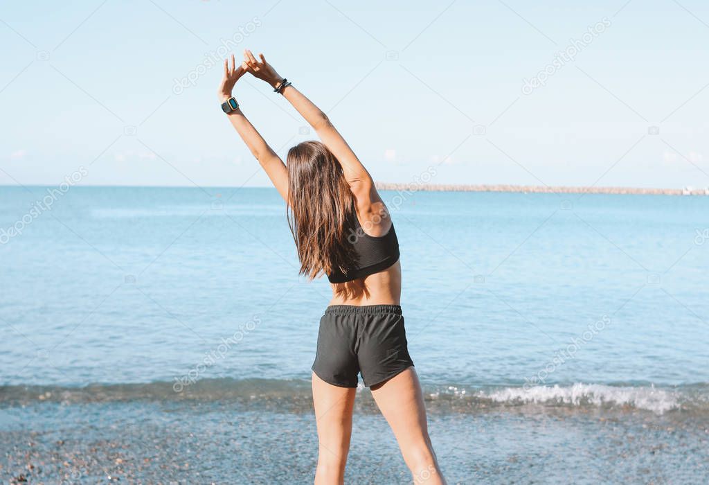 Young slim athletic long hair woman in sportswear doing exercises on the sea beach in morning, healthy lifestyle