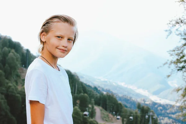 Blonde lächelnde Junge schaut in die Kamera vor dem Hintergrund der wunderbaren Aussicht auf Bergresort, Familienreise Abenteuer Lebensstil — Stockfoto