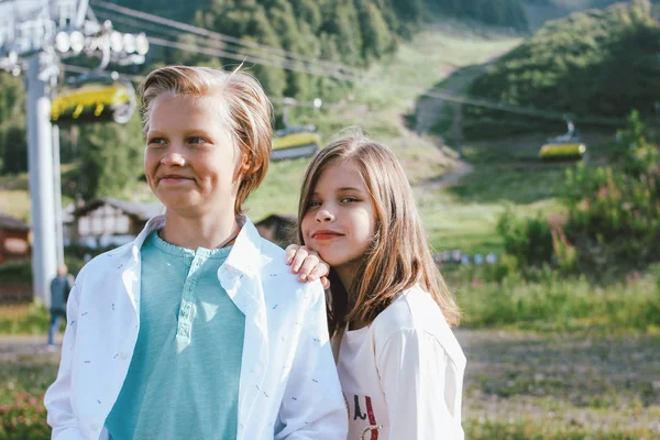 Cute children brother and sister friends against background of mountain resort, family travel adventure concept — Stock Photo, Image