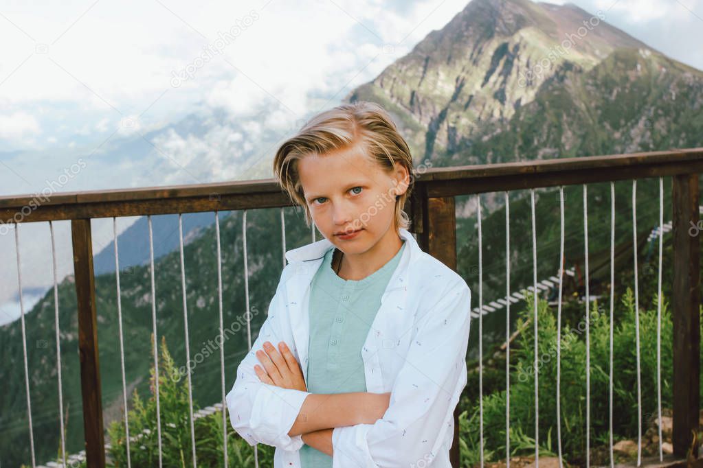 Blonde boy on observation deck on background of wonderful view of mountain resort, family travel adventure lifestyle