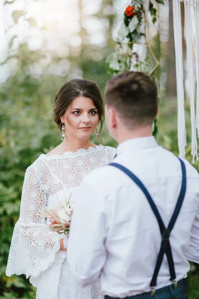 Schöne lächelnde Braut brünette junge Frau mit dem Boho-Stil Strauß mit Bräutigam auf Hochzeitszeremonie im Wald — Stockfoto