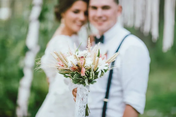 Szczęśliwa Świeżo poślubiona para z bukietem w stylu boho na ceremonii ślubnej w lesie. Selektywne skupienie na kwiatach — Zdjęcie stockowe