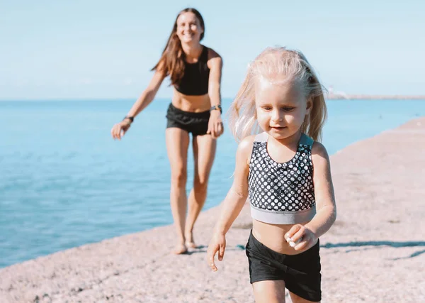 Маленькая симпатичная девочка ищет подходящую маму на пляже, здоровый образ жизни, спортивная семья — стоковое фото