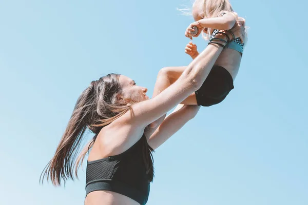Young fit woman mom with little cute girl exercising on beach together, healthy lifestyle, dynamic gymnastic