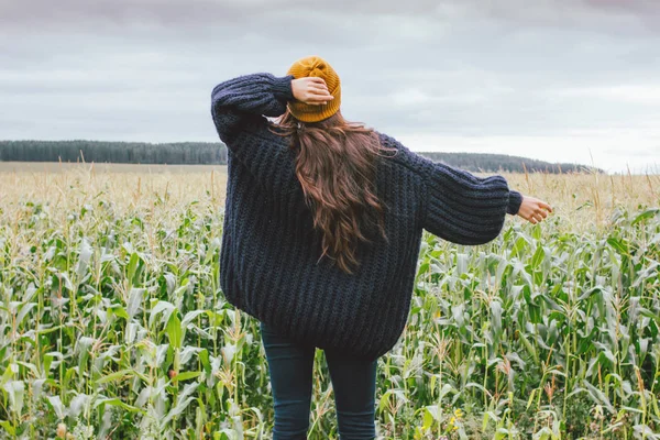 Длинные волосы, девушка в желтой шапке и вязаном свитере сзади на осеннем кукурузном поле. Чувствительность к природе — стоковое фото