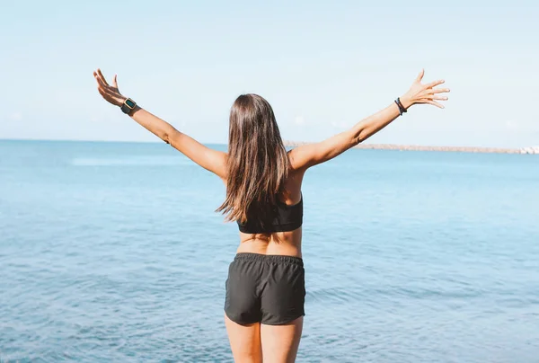 Jeune femme mince et athlétique aux cheveux longs en vêtements de sport faisant des exercices sur la plage de la mer le matin, mode de vie sain — Photo