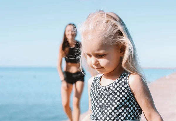 Маленькая симпатичная девочка бежит к маме на пляж, здоровый образ жизни, спортивная семья — стоковое фото