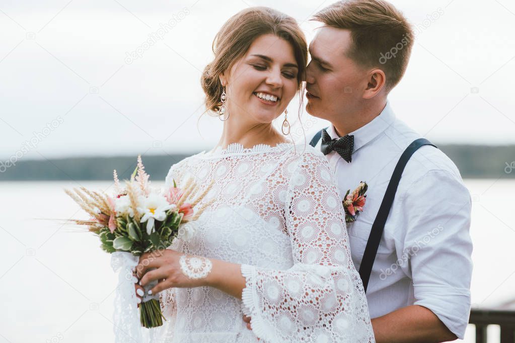 Happy newly married couple, smiling bride brunette young woman with boho style bouquet with groom, outdoors