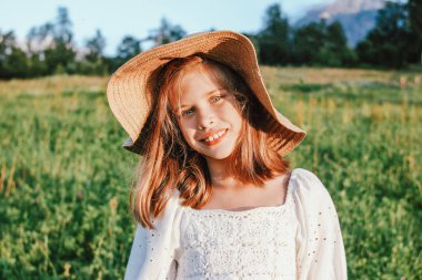 Dağda güzel evlerin arka planına karşı hasır şapka güzel romantik preteen kız, gün batımında kırsal sahne