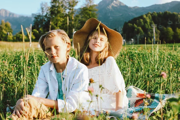 Children brother and sister friends sitting in grass against the background of beautiful mountains, family travel, rural scene — Stock Photo, Image