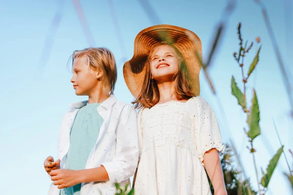 Lachende kinderen broer en zus vrienden in gras op de achtergrond van blauwe hemel, landelijke scène — Stockfoto