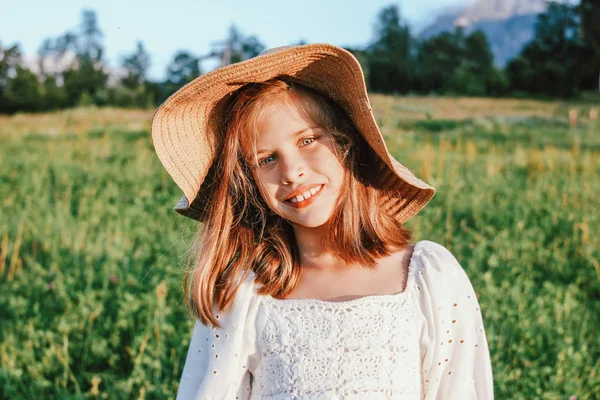 Linda menina pré-adolescente romântica em chapéu de palha contra o fundo de belas casas na montanha, cena rural ao pôr do sol — Fotografia de Stock
