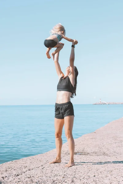 함께 해변에서 운동하는 작은 귀여운 소녀와 젊은 적합 여성 엄마, 건강한 라이프 스타일, 동적 체조 — 스톡 사진