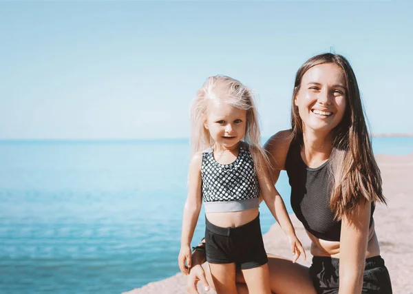 Jeune femme en forme maman avec une petite fille mignonne faisant de l'exercice sur la plage de la mer ensemble, mode de vie sain — Photo