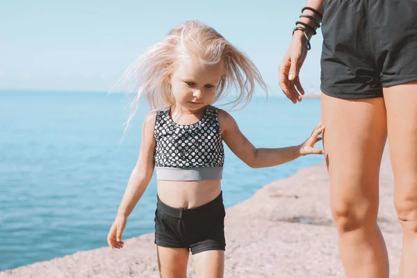 해변, 건강한 라이프 스타일, 스포츠 가족에 맞는 엄마의 배경에 카메라를보고 작은 귀여운 소녀 — 스톡 사진