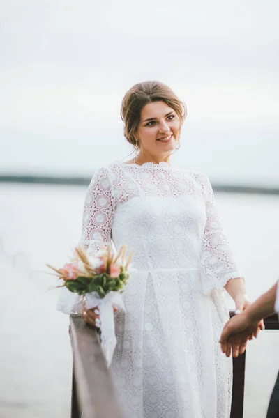 Feliz casal recém-casado, sorrindo noiva morena jovem com o buquê estilo boho olhando para o noivo, ao ar livre — Fotografia de Stock