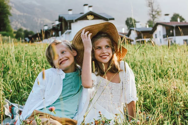 Children brother and sister friends sitting in grass against background of beautiful houses in mountain, family travel, rural scene — Stock Photo, Image