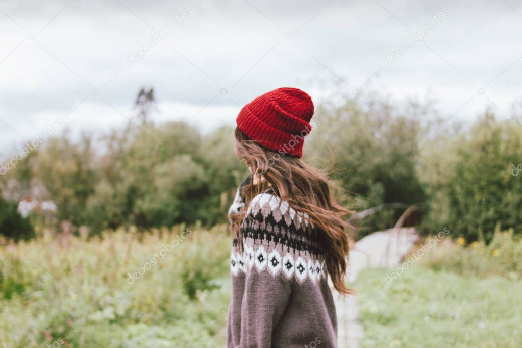 Beautiful carefree long hair asian girl in the red hat and knitted nordic sweater from behind in autumn nature park