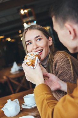 Mutlu genç çift birlikte kafede oturan sıcak rahat giyim giymiş. Adam kız kruvasan besler