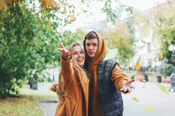 Счастливая молодая пара влюбленных подростков друзья одеты в случайный стиль ходить вместе и бросает листья на камеру, осень улице города — стоковое фото