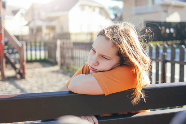 Грустная одинокая девочка-подросток, сидящая на скамейке на детской площадке — стоковое фото