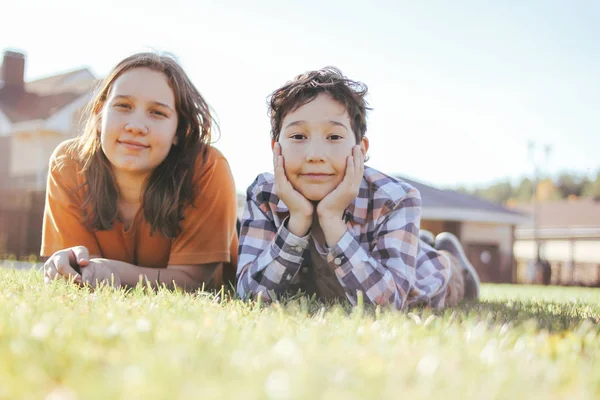Lachende kinderen broer en zus liggen op zonnig groen gras van cottage dorp op de achtergrond — Stockfoto