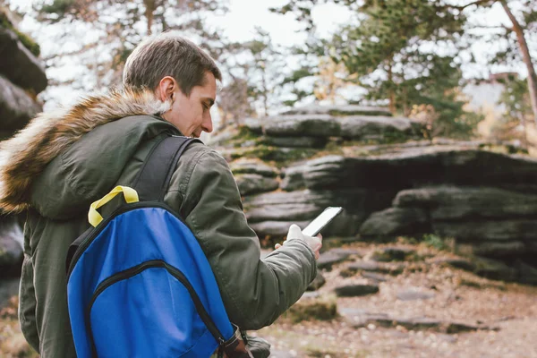 Jovem viajante do sexo masculino em jaqueta cáqui parka com mochila olha para a rota em seu telefone móvel, estilo de vida de aventura de viagem — Fotografia de Stock