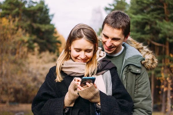 Glückliches junges verliebtes Paar im Freizeitlook mit Handy auf Naturparkwald unterwegs — Stockfoto