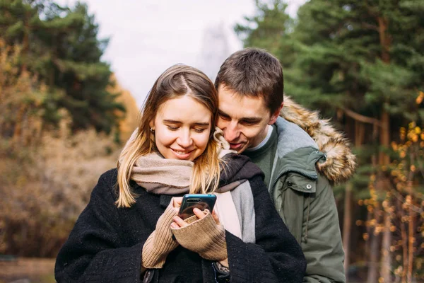 Feliz joven pareja enamorada amigos viajeros vestidos con estilo casual utilizando el móvil en el bosque del parque natural — Foto de Stock