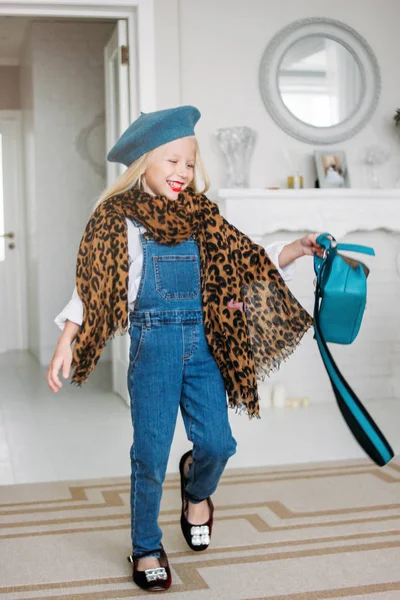 Cute fashion trendy fair hair little girl dressed in denim overalls, leopard scarf and blue beret with mom's accessories. Daughter imitates mom — Stock Photo, Image