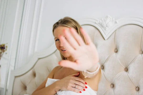 Gelukkig glimlachen mooie lange haar jonge vrouw trekken hand in de richting van de camera zitten op bed, selectieve focus op de hand — Stockfoto