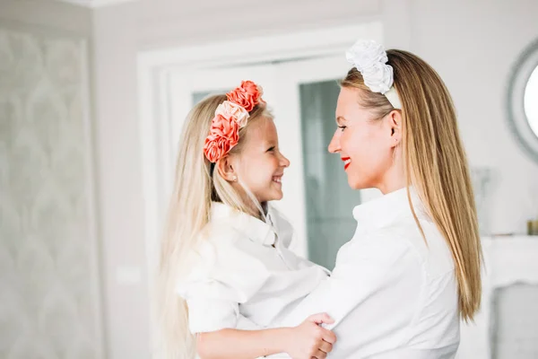 Glücklich blondes langes Haar Mutter und süße Tochter in Blumenkränzen im Wohnzimmer, glückliches Familienleben — Stockfoto