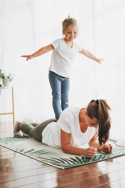 Happy mom and little daughter doing morning exercise together at bright interior home