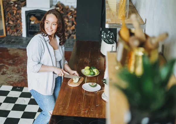 Volwassen Glimlachen Brunette Vrouw Casual Kleding Snijdt Avocado Keuken Thuis — Stockfoto