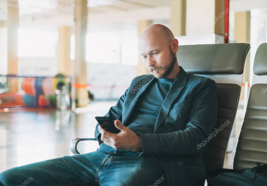 Handsome bald bearded man businessman in suit using mobile phone at airport lounge