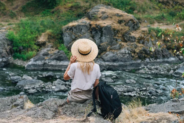 Νεαρή Γυναίκα Ταξιδιώτη Ψάθινο Καπέλο Σακίδιο Κάθεται Και Κοιτάζει Βουνό — Φωτογραφία Αρχείου