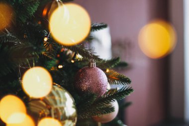 Altın ve mor oyuncaklarla süslenmiş Noel ağacı. Işıklar bokeh desenli arka plan.