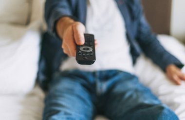 Adamın elinde uzaktan kumanda var, yatak odasında uzanmış, seçici odaklanma.