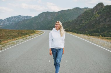 Güzel, gülümseyen sarışın genç kadın yoldaki beyaz kapüşonlu gezgin, dağlara yolculuk, Altai