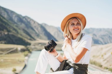 Güzel, gülümseyen, sarışın, keçeli şapkalı, elinde fotoğraf makinesi olan genç bir kadın gezgin Altai dağlarına seyahat ediyor.