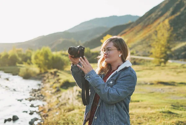 Elinde fotoğraf makinesi olan güzel, gülümseyen sarışın genç bir gezgin. Dağlara yolculuk.
