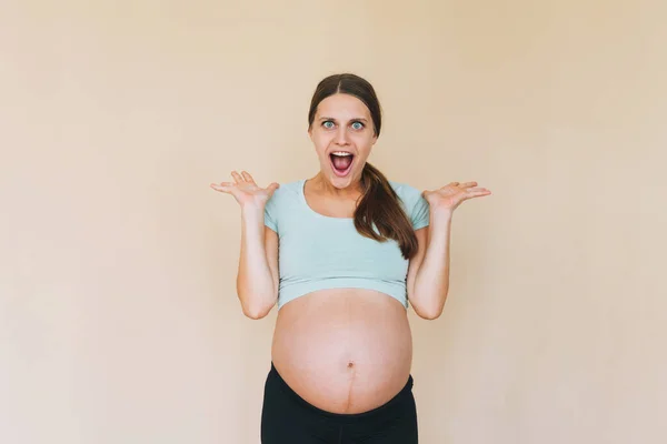 若いです驚くべき妊娠中の女性でスポーツウェア絶縁でベージュ背景 — ストック写真